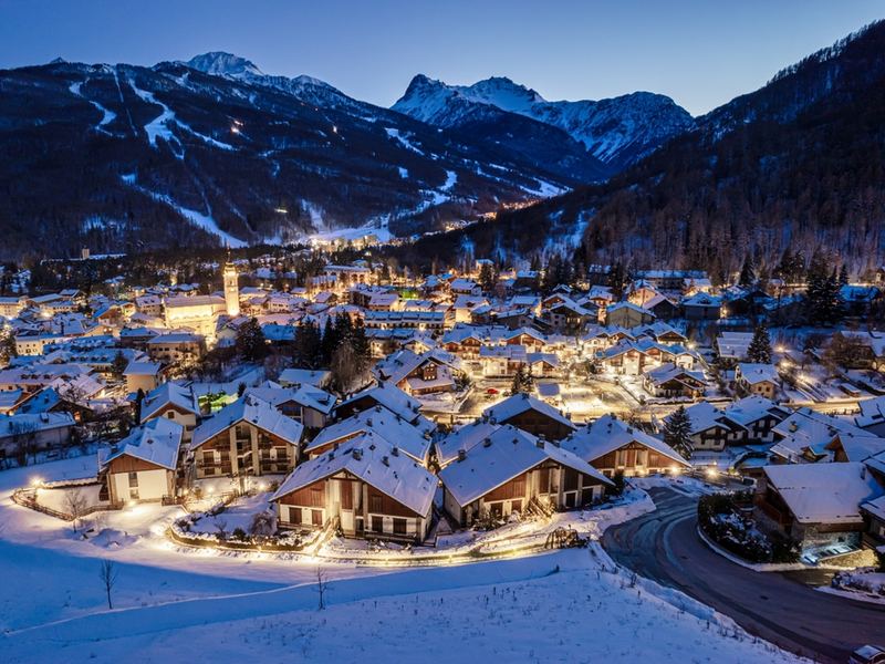 An Alpine resort village lit up at dusk, with the road winding in