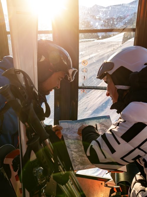 Two skiers in a gondola planning their route on a piste map
