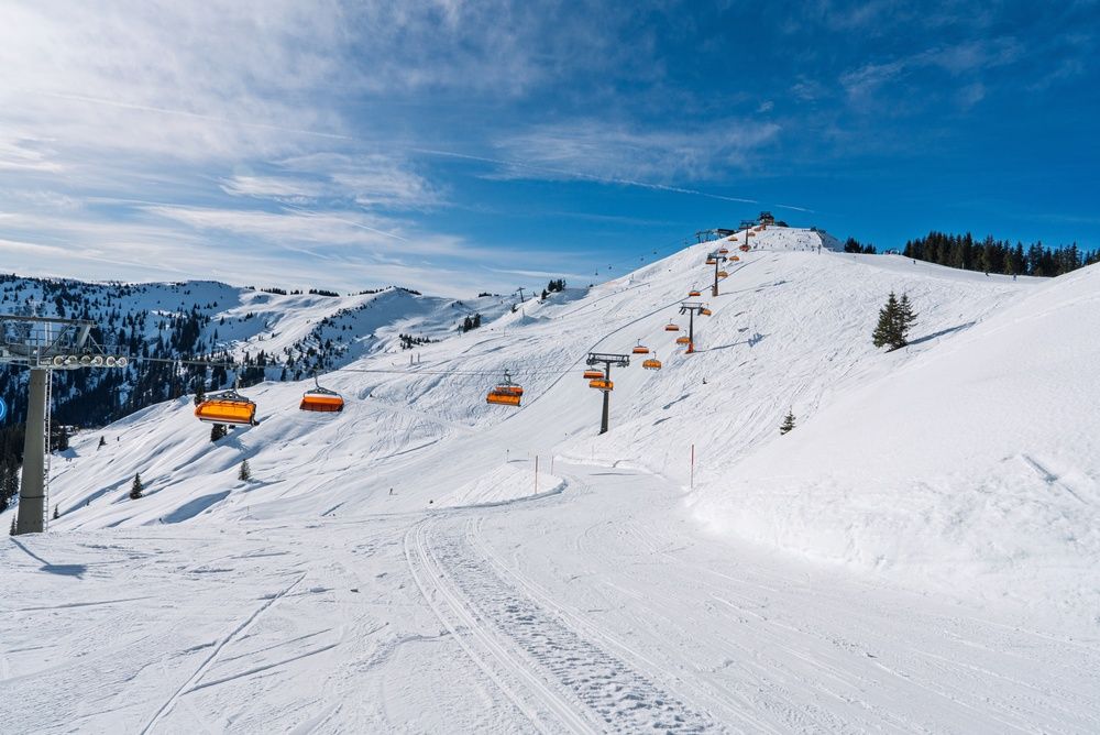 Empty orange chairlifts climbing a sunny, snow-covered slope under a blue sky
