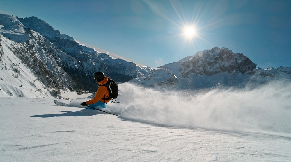 A skier carving through fresh snow beneath sunlit Alpine peaks